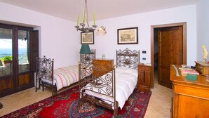A bedroom with a bed, a chair, a dresser, a chandelier, and a view through a glass door. - Villa Acquavella (Casal Velino)