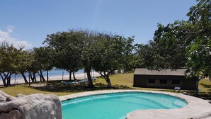 A swimming pool with a slide, surrounded by trees and a small building. - Serenity Nhabanga (Praia do Bilene)