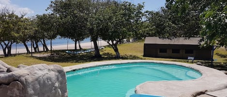 Una piscina con tobogán, rodeada de árboles y un pequeño edificio.