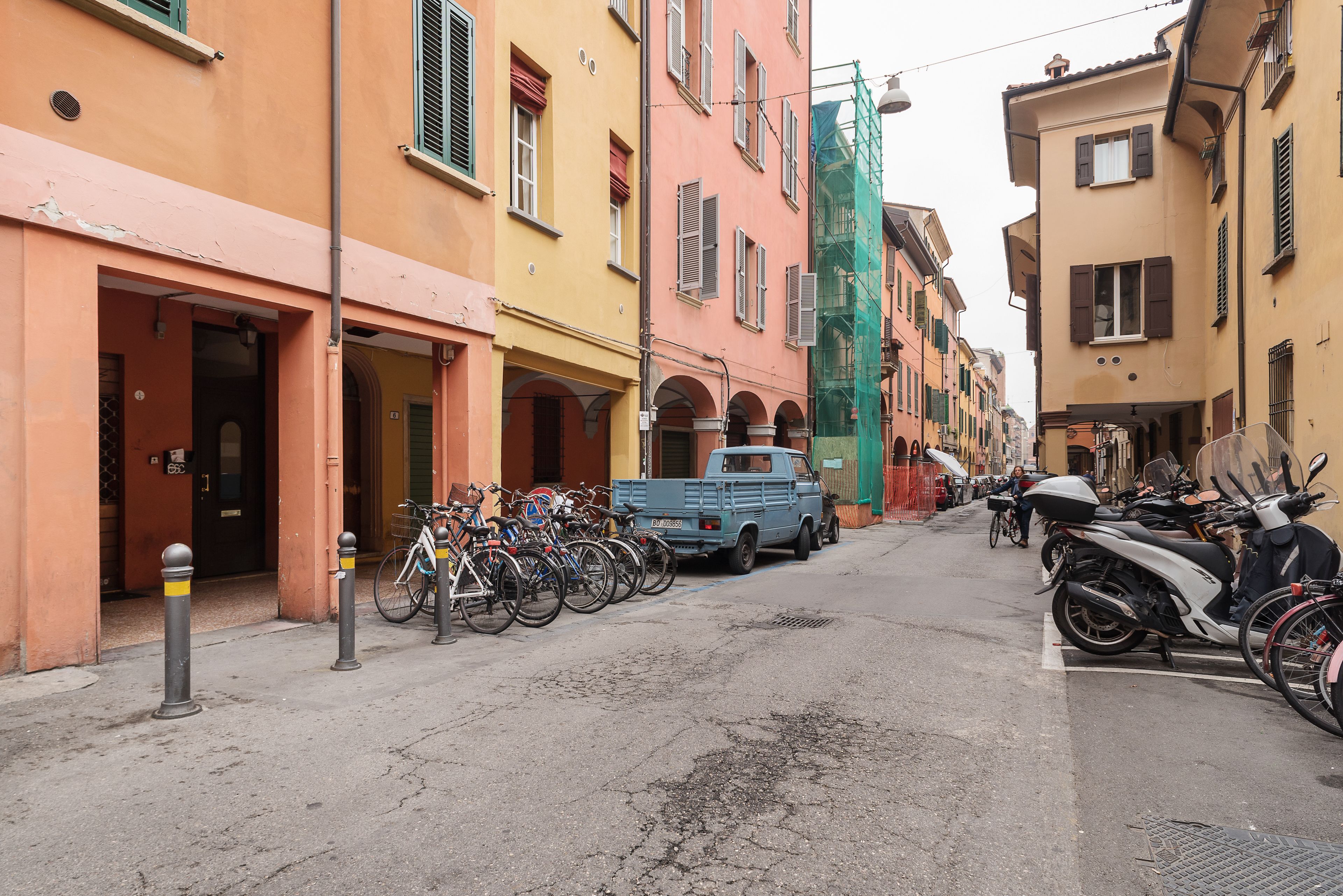 En smal gata kantad av färgglada byggnader, parkerade cyklar och en blå lastbil.