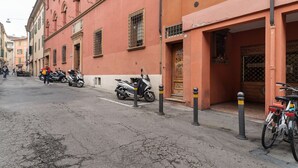 Una calle con motocicletas y bicicletas estacionadas, edificios con ventanales arqueados, y una puerta con reja de metal.
