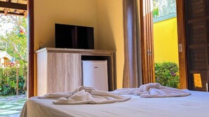 A hotel room with a bed, a television on a wooden cabinet, and a sliding door leading to an outdoor area. - Recanto das Tiribas (Ilhabela)