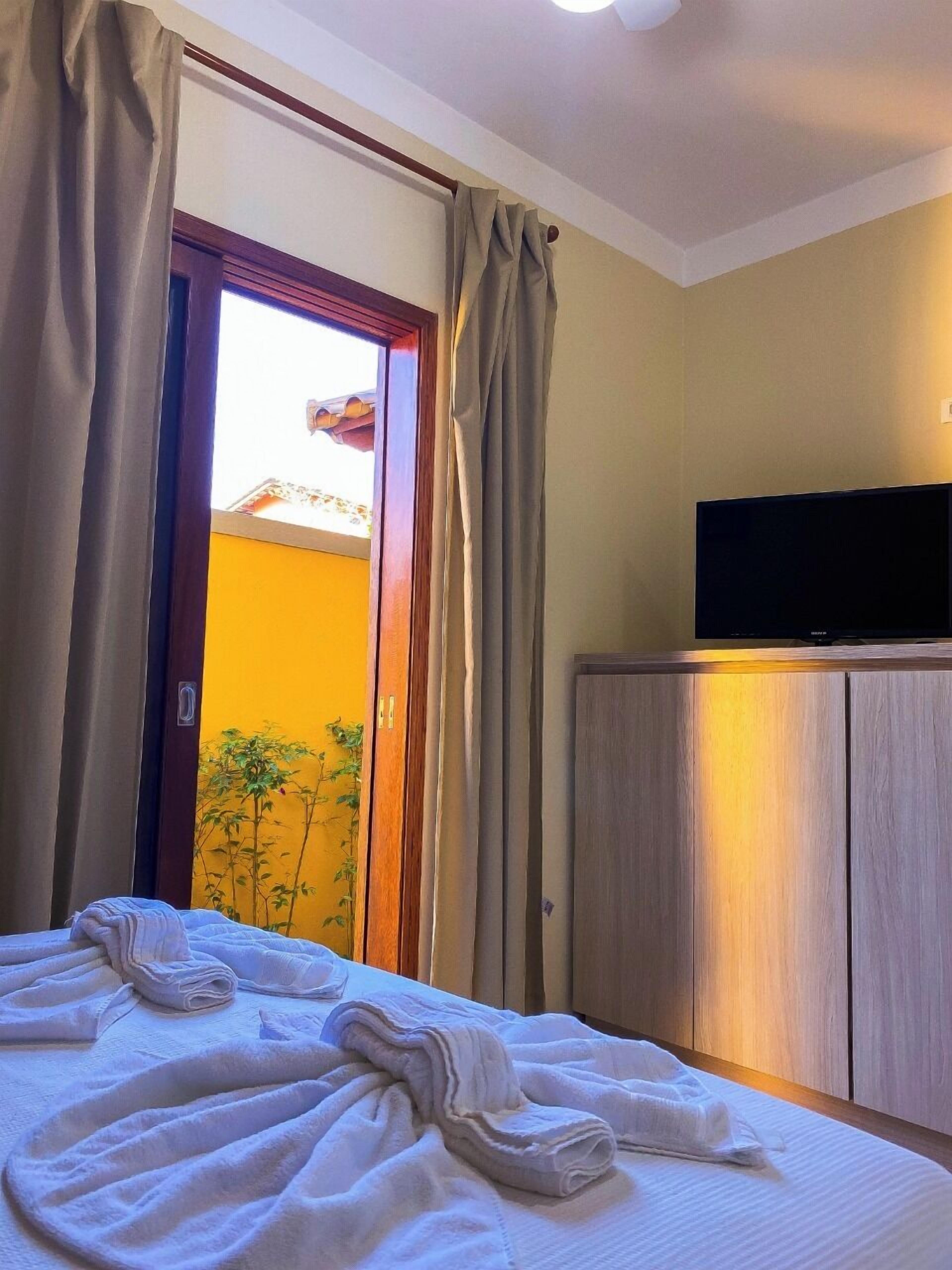 A hotel room with a bed, a television on a wooden cabinet, and a view of a yellow wall and a door leading outside.