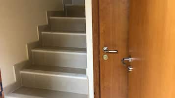 Una puerta de madera con un picaporte plateado y un ojo de cerradura, que da acceso a una escalera con escalones blancos.