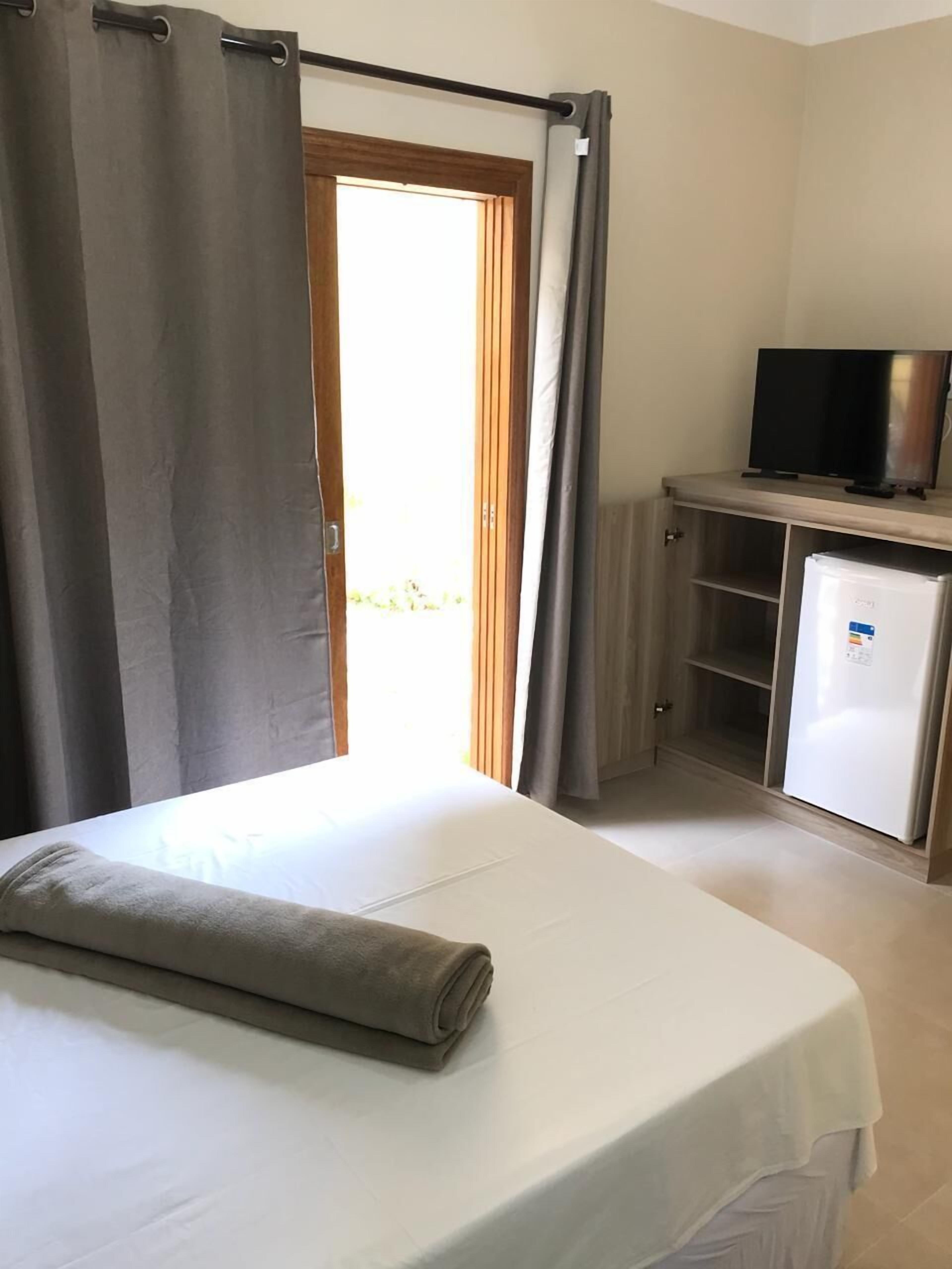 Una habitación con una cama, un televisor en un mueble y un refrigerador.