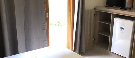 Una habitación con una cama, un televisor en un mueble y un refrigerador.
