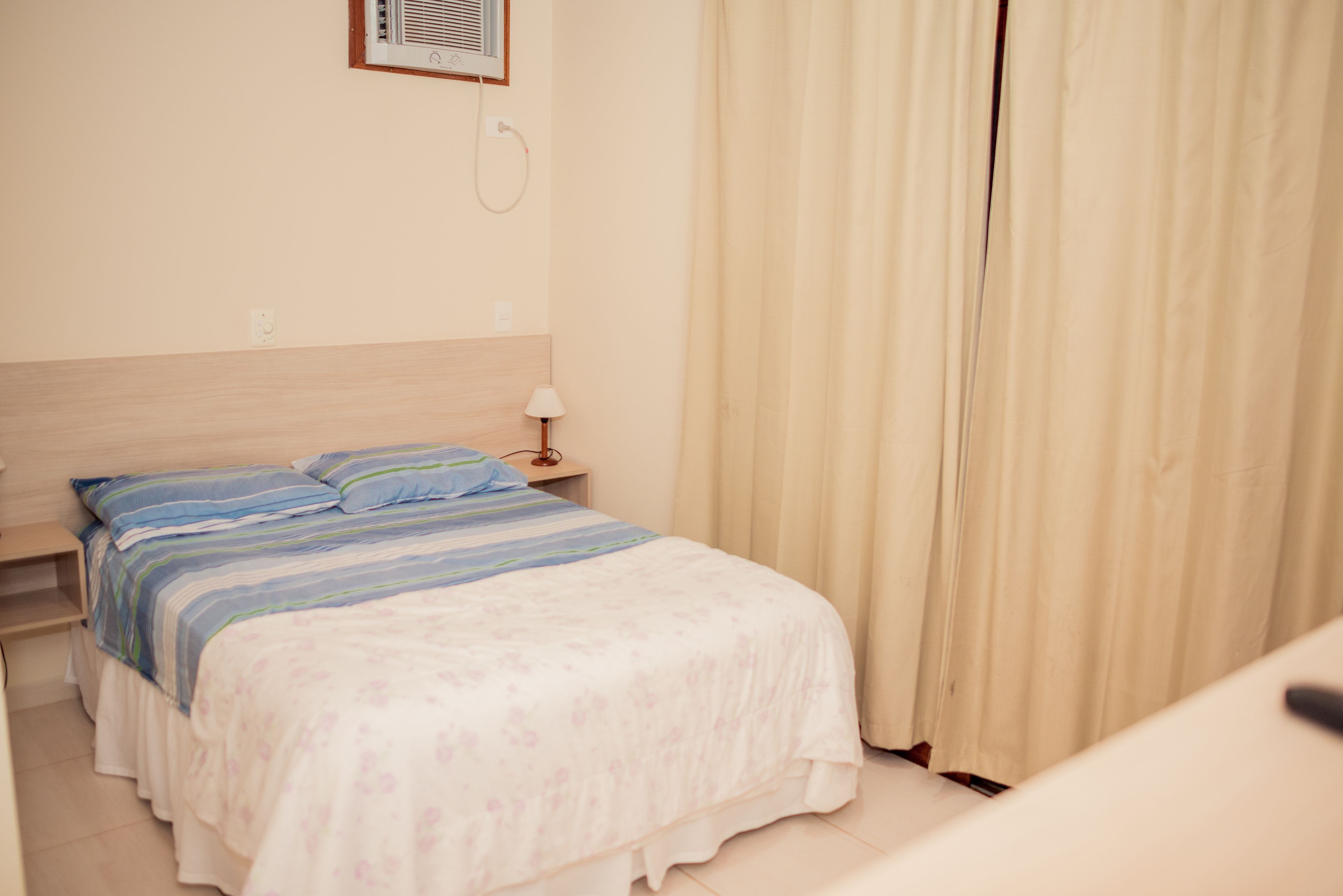 A bedroom with a bed, a nightstand, a lamp, and a window with curtains.