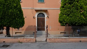 A building with a large wooden door, a brick wall, and a metal fence. - Marconi Airport Cozy Dream Flat (Bologna)