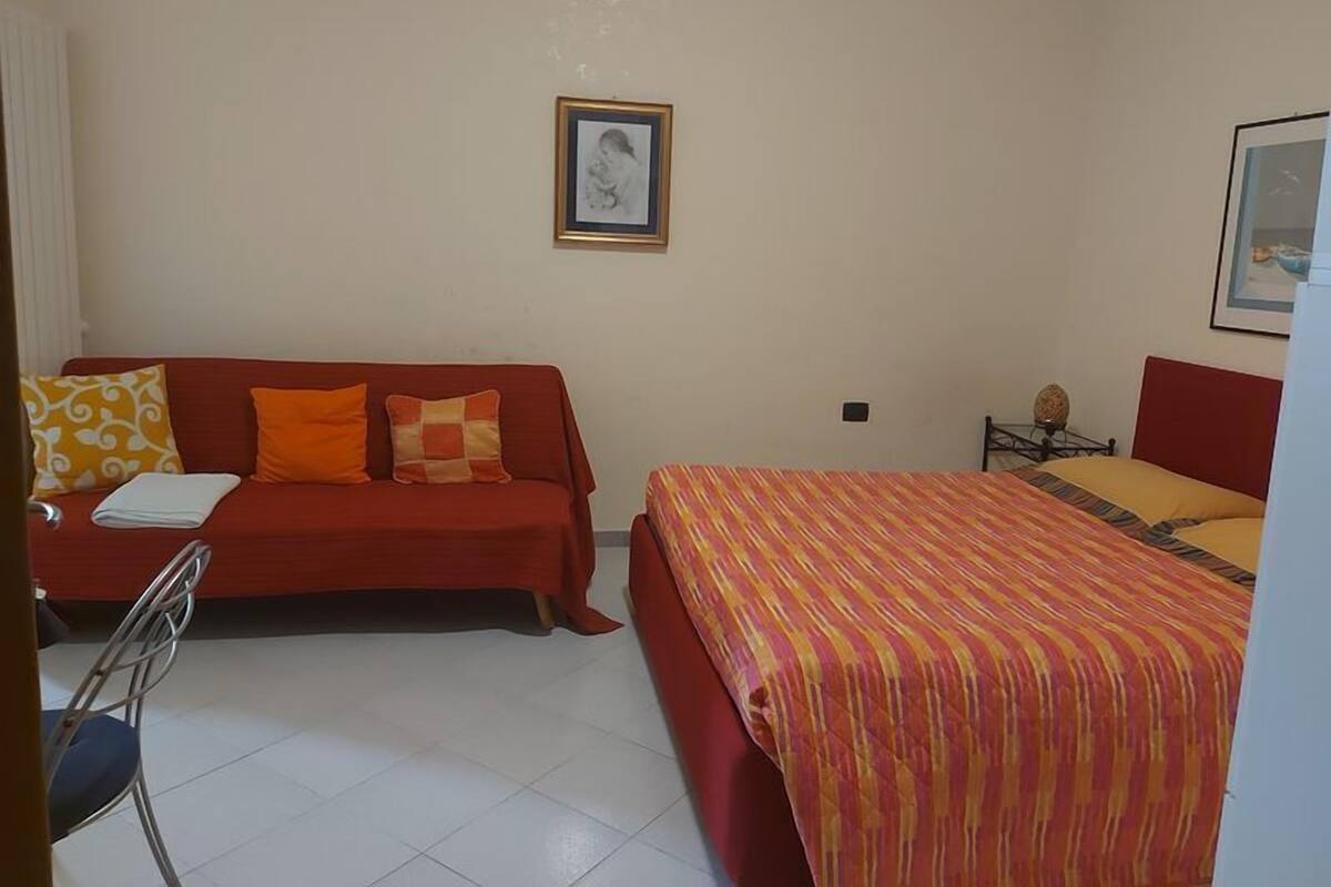 A room with a red sofa, a bed with a striped bedspread, and a framed picture on the wall.
