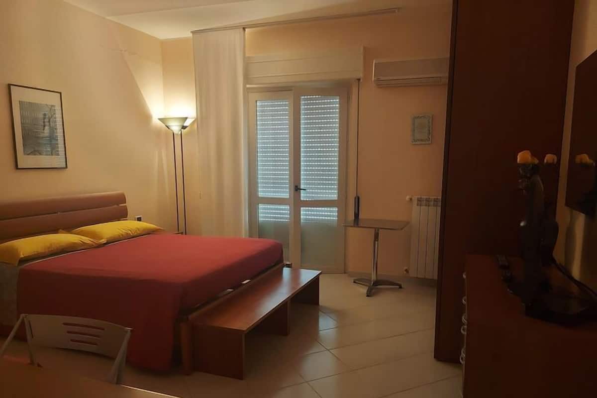A hotel room with a bed, bedside table, chair, and a desk.