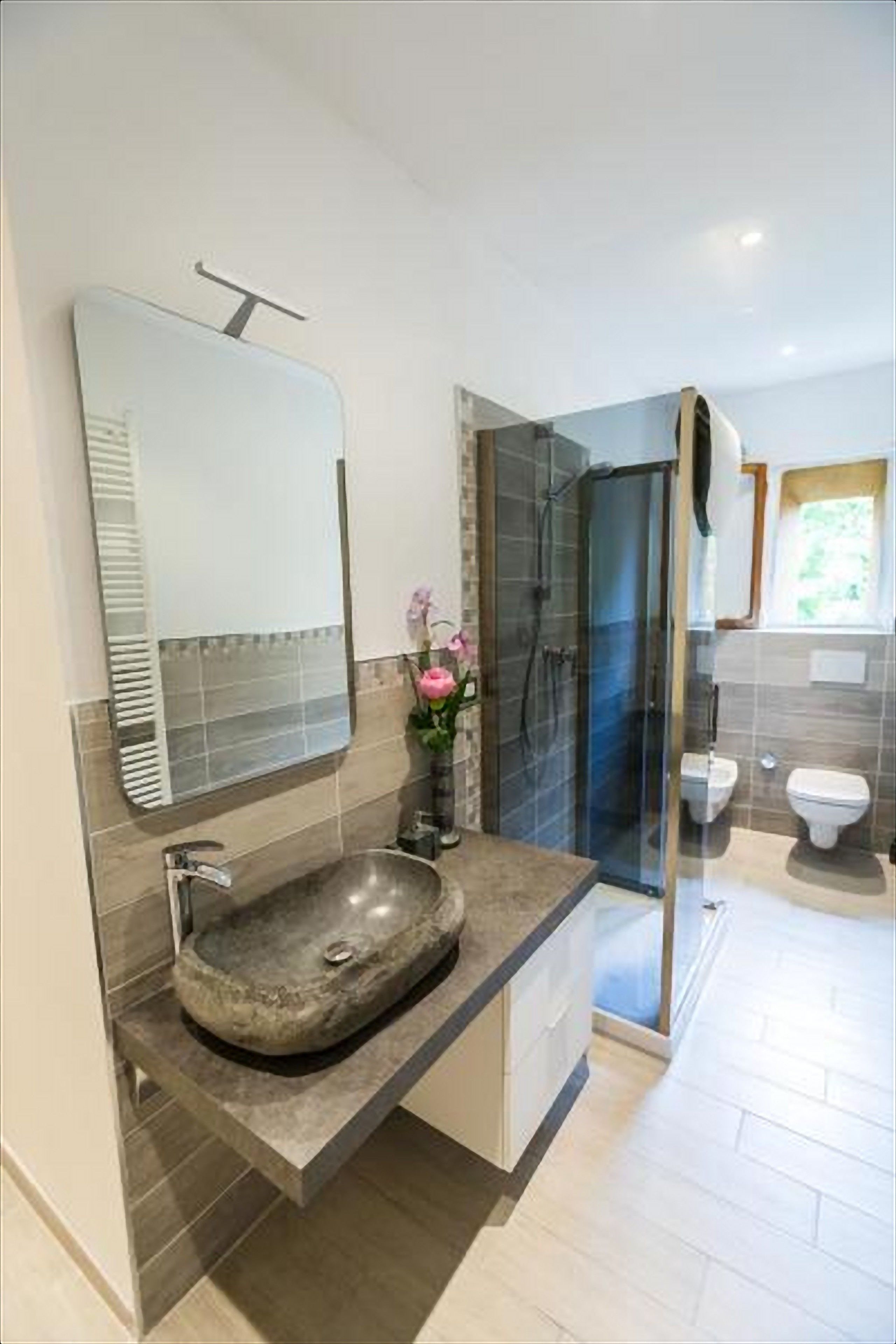 Une salle de bain moderne avec un lavabo en pierre, une douche en verre et un grand miroir.