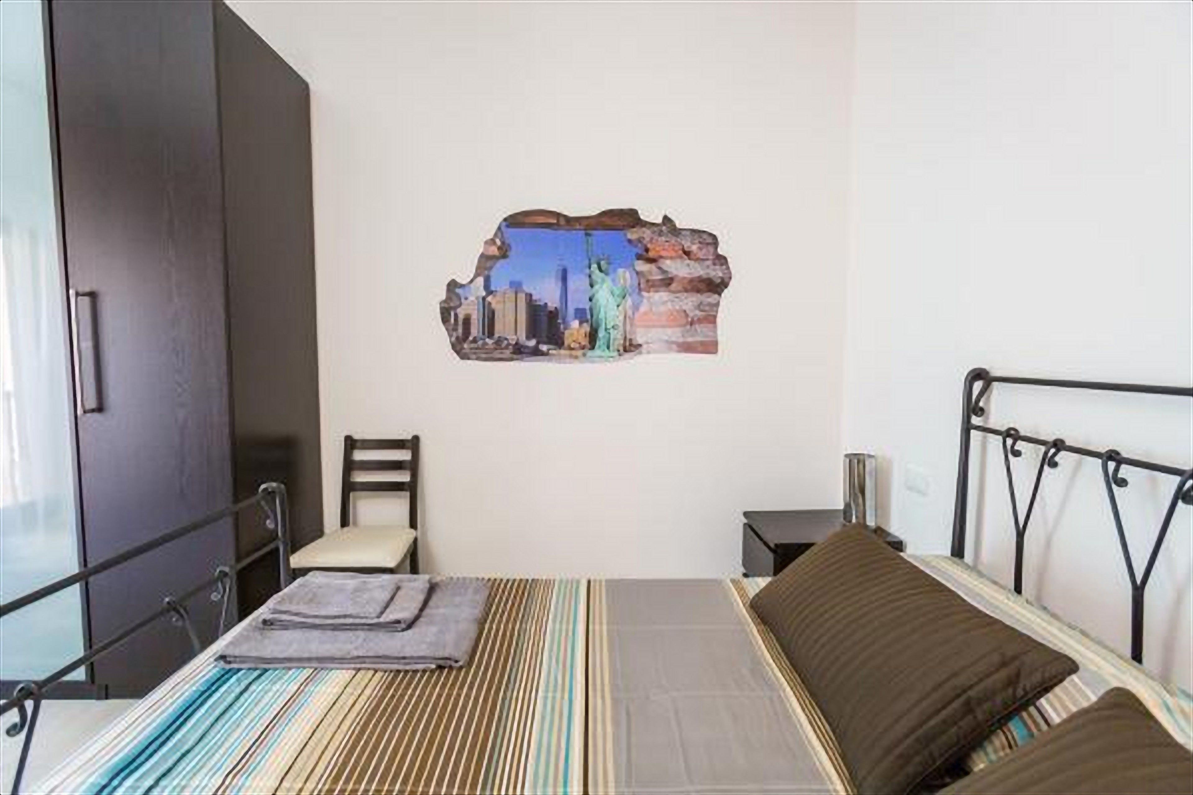 Un dormitorio con cama, una silla, una mesita de noche y un adorno en la pared.