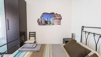 Un dormitorio con cama, una silla, una mesita de noche y un adorno en la pared.