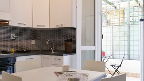 Une cuisine moderne avec des meubles blancs, un dosseret en carreaux noirs et un coin repas comprenant une table et des chaises.
