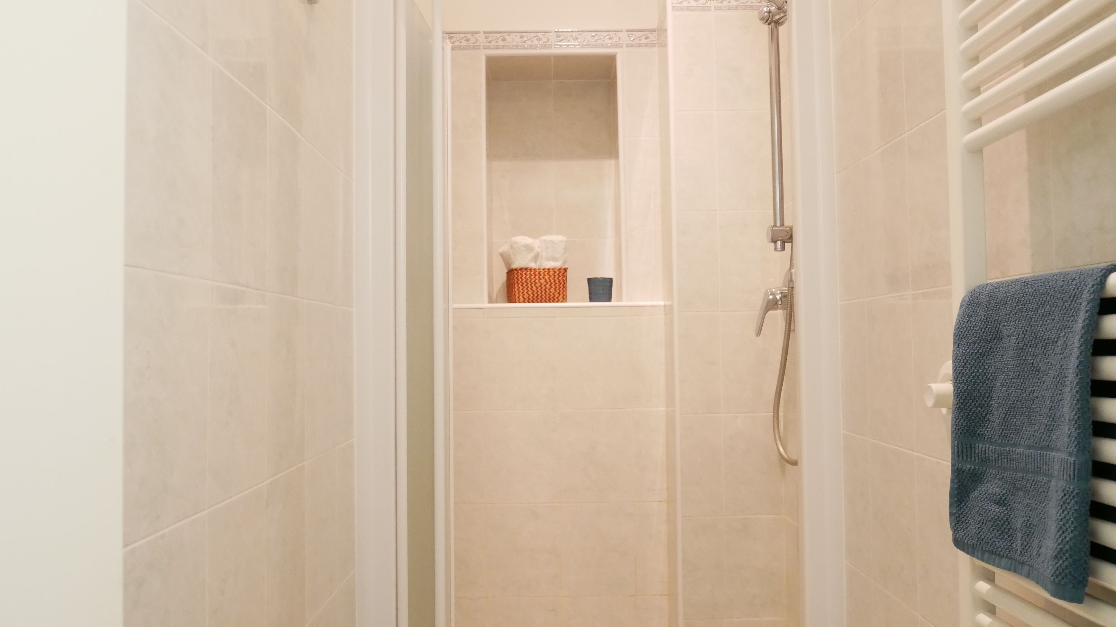 Un piccolo spazio doccia con piastrelle beige, un porta asciugamani e uno scaffale con articoli da toilette.