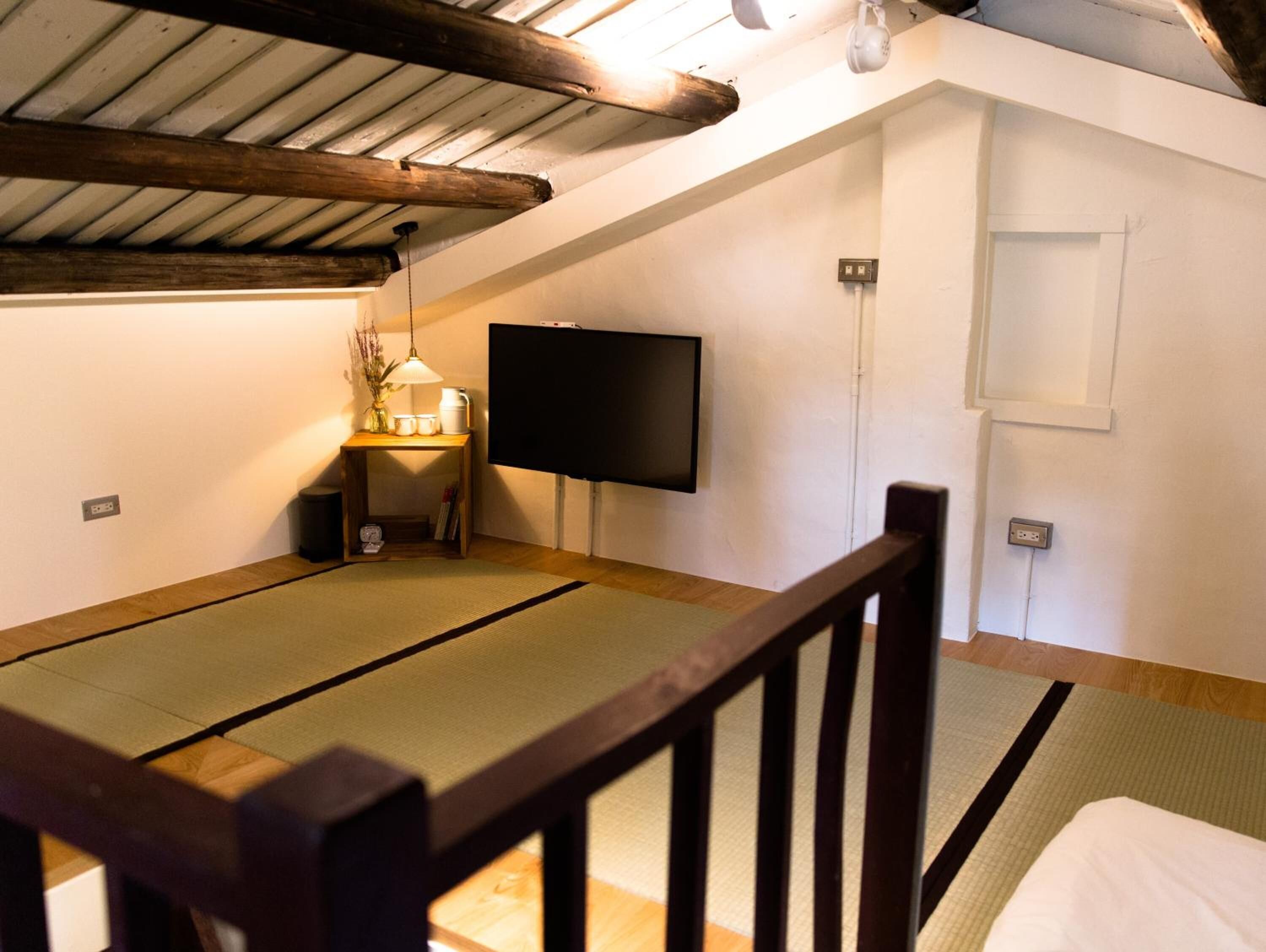 A tatami mat room with a television, a small table with a lamp, and a wooden chair.
