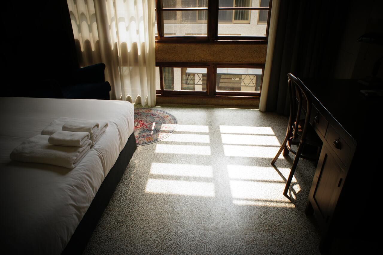A hotel room with a bed, a desk, and a view through a window.