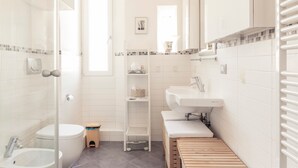 Ein modernes Badezimmer mit Duschkabine aus Glas, Toilette, Waschbecken und einer kleinen Holzbank.