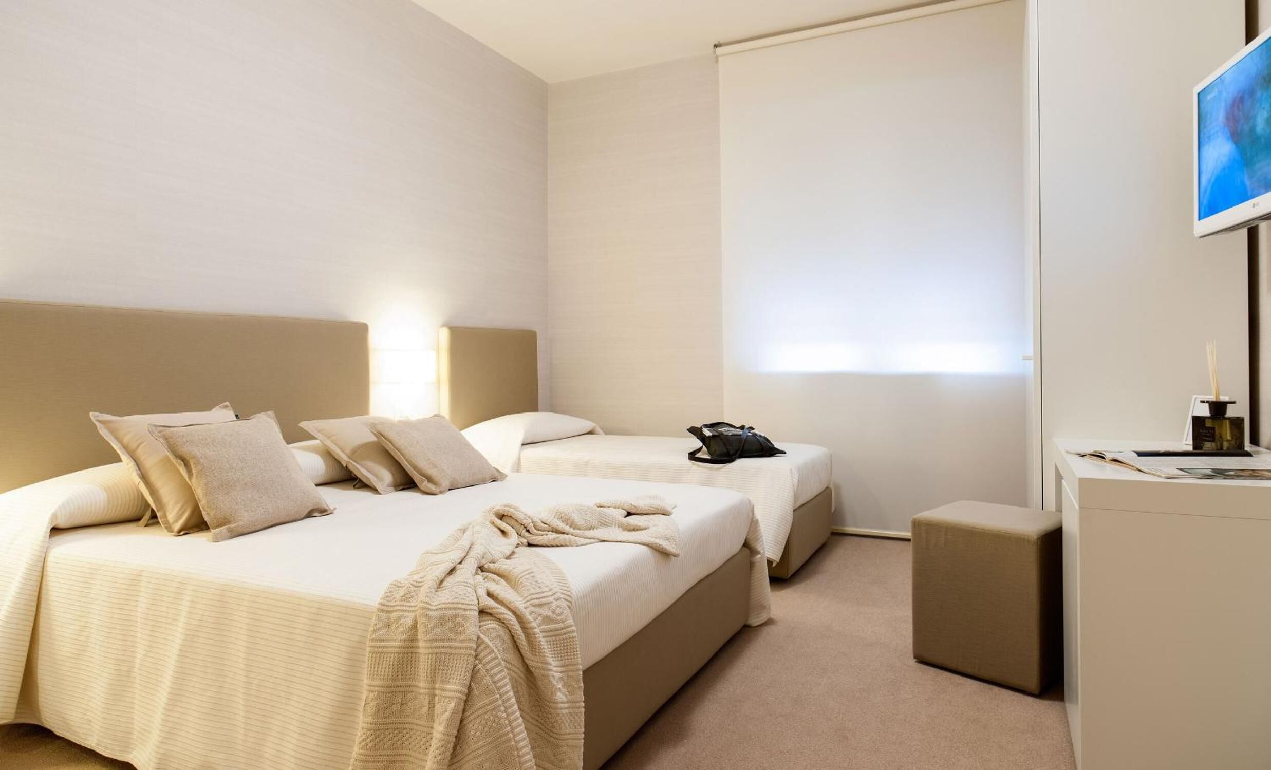 Ein Hotelzimmer mit zwei Betten, einem Schreibtisch, einem Stuhl, einem Fernseher und einem Fenster mit Jalousien.