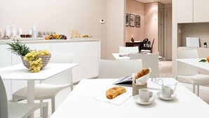 Ein moderner Hotel-Speisesaal mit weißen Möbeln, einer Obstschale und einem Croissant auf dem Tisch.