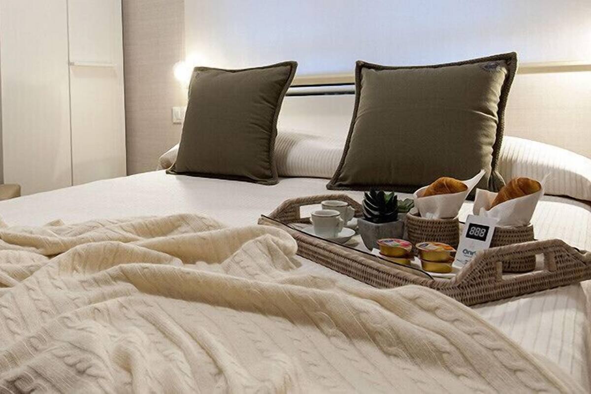 A neatly made bed with a white blanket, two pillows, and a tray with breakfast items.