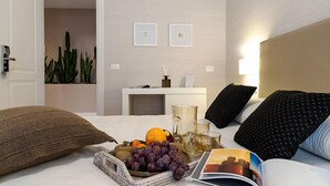 Ein ordentlich eingerichtetes Hotelzimmer mit einem Bett, einem Nachttisch mit Lampe, einem kleinen Schreibtisch und einem an der Wand befestigten Regal.