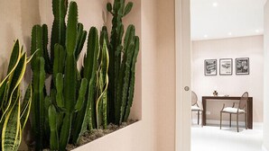 Eine Dekoration aus Kakteenpflanzen im Flur, ein Empfangsschalter mit Sitzgelegenheiten und gerahmte Bilder an der Wand.