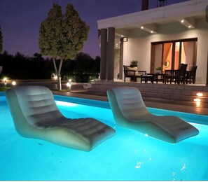 Ein Swimmingpool mit zwei Liegestühlen, einer modernen Sitzgelegenheit im Freien und einem Baum.