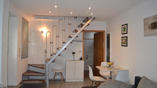 A modern living room with a staircase, a dining area, and a kitchen. - Ferienwohnung Resit 1 (Wunstorf)