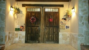 Une porte en bois rustique ornée d’une guirlande, des murs en pierre et des panneaux indiquant « casa rural » et « TRINO ».