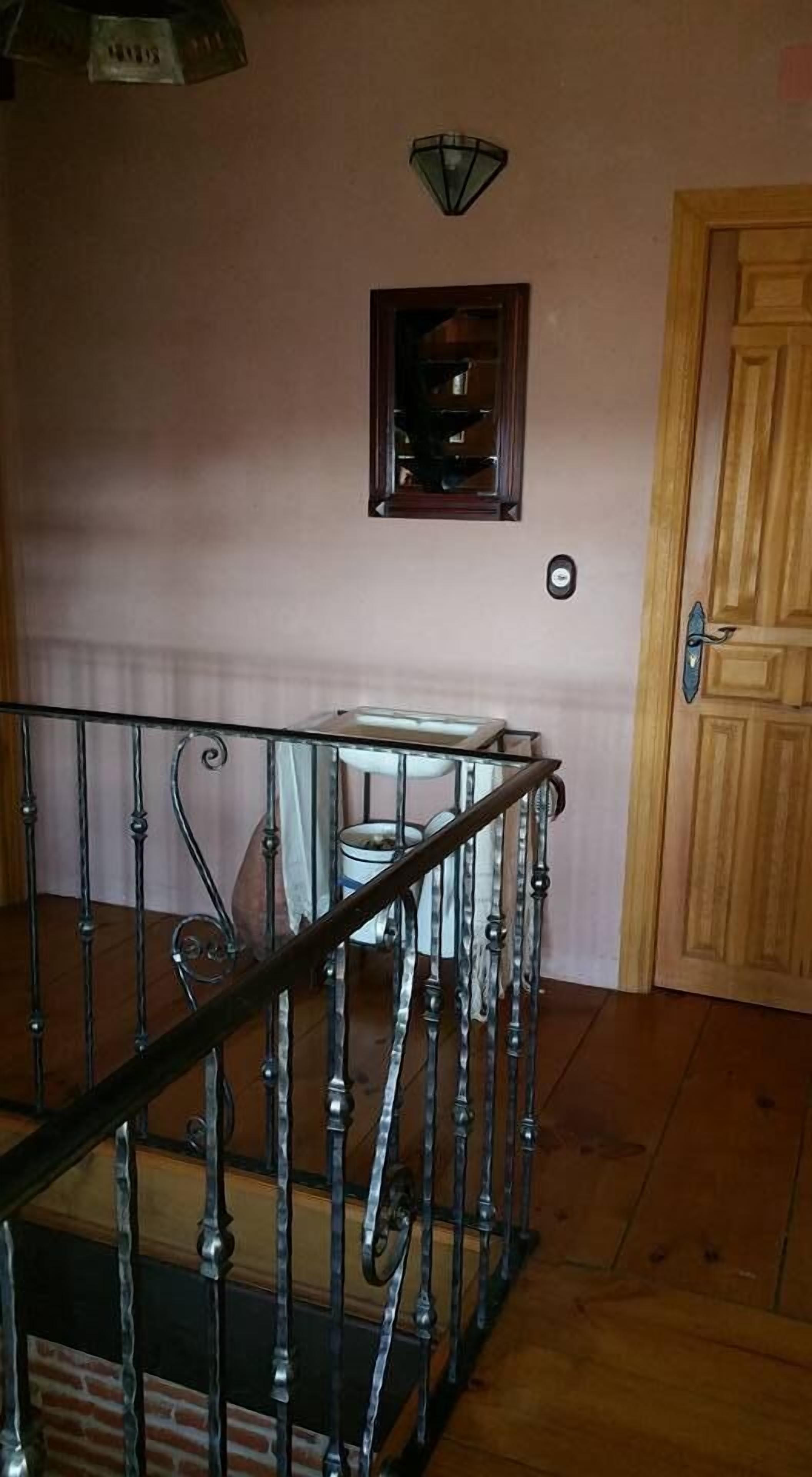 Una escalera con barandilla metálica, una puerta de madera y un ventanal pequeño con una lámpara arriba.