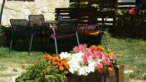 Un espace extérieur aménagé avec des sièges, un parasol rouge, un mur en pierre et un jardinier.