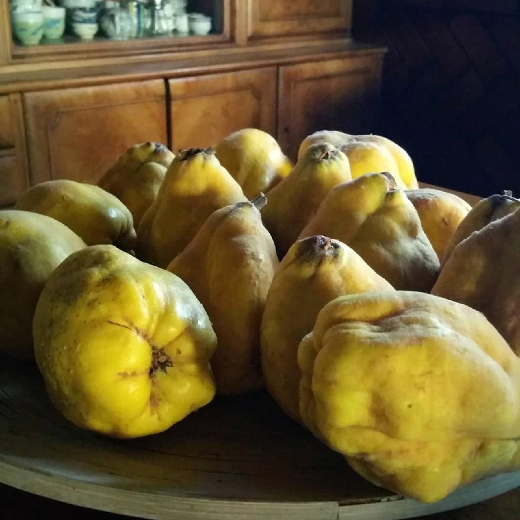A wooden table with a bowl containing several yellow fruits.