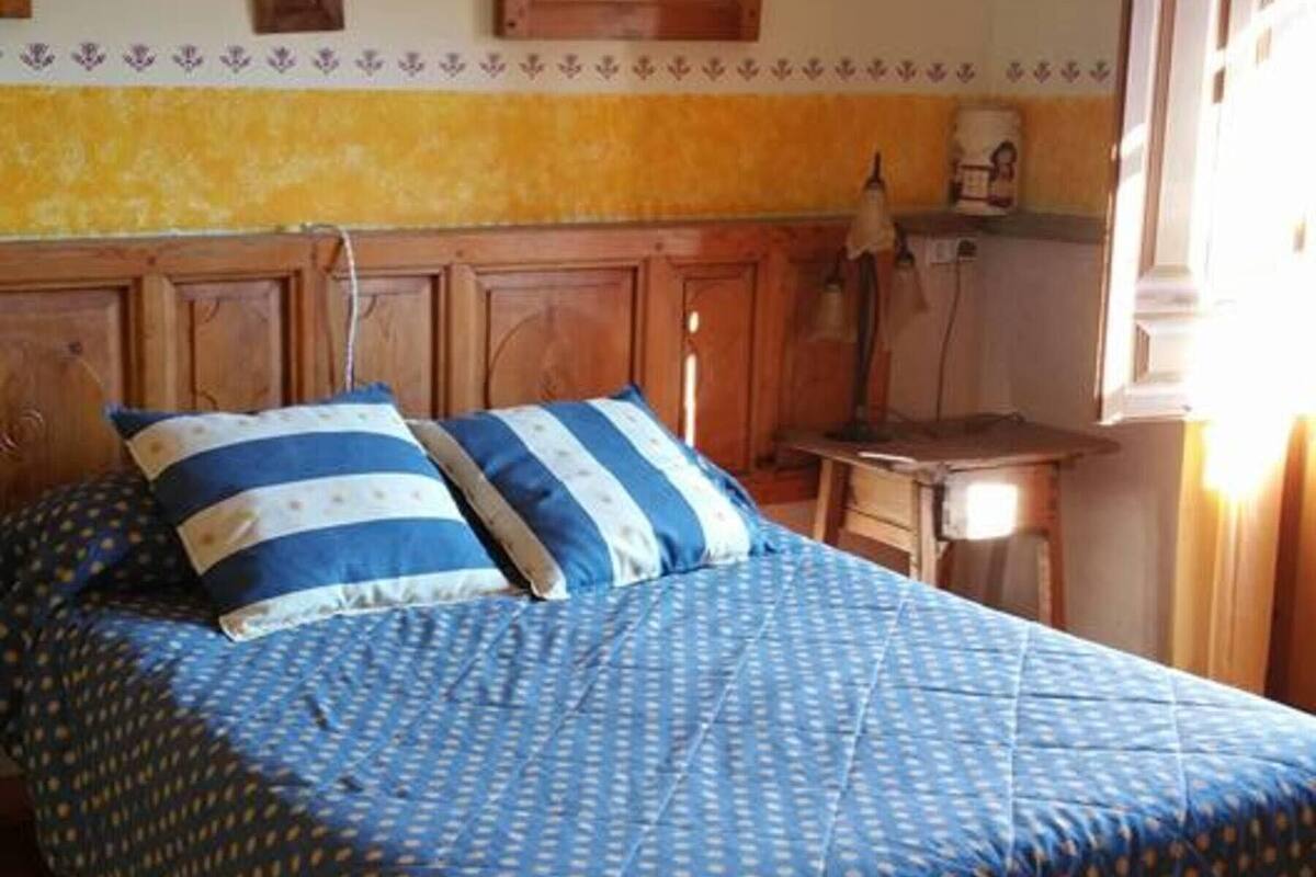 A bed with a blue and white patterned bedspread and pillows, wooden headboard, and a wooden floor.