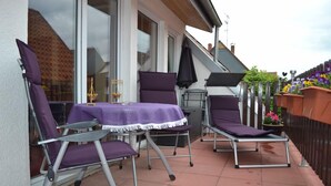 An outdoor patio with a table and two chairs, a sun lounger, and a small table with a candle. - Ferienwohnung Resit 2 (Wunstorf)