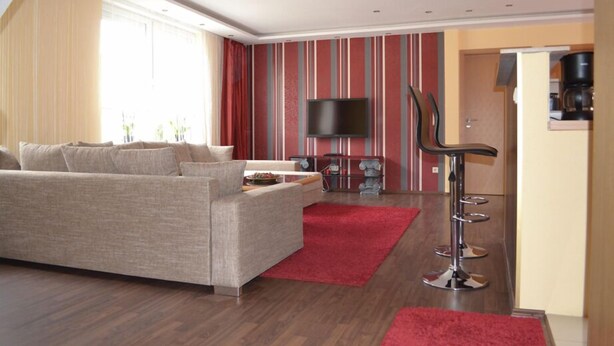 A modern living room with a sofa, a TV, a coffee machine, and a red rug. - Ferienwohnung Resit 2 (Wunstorf)