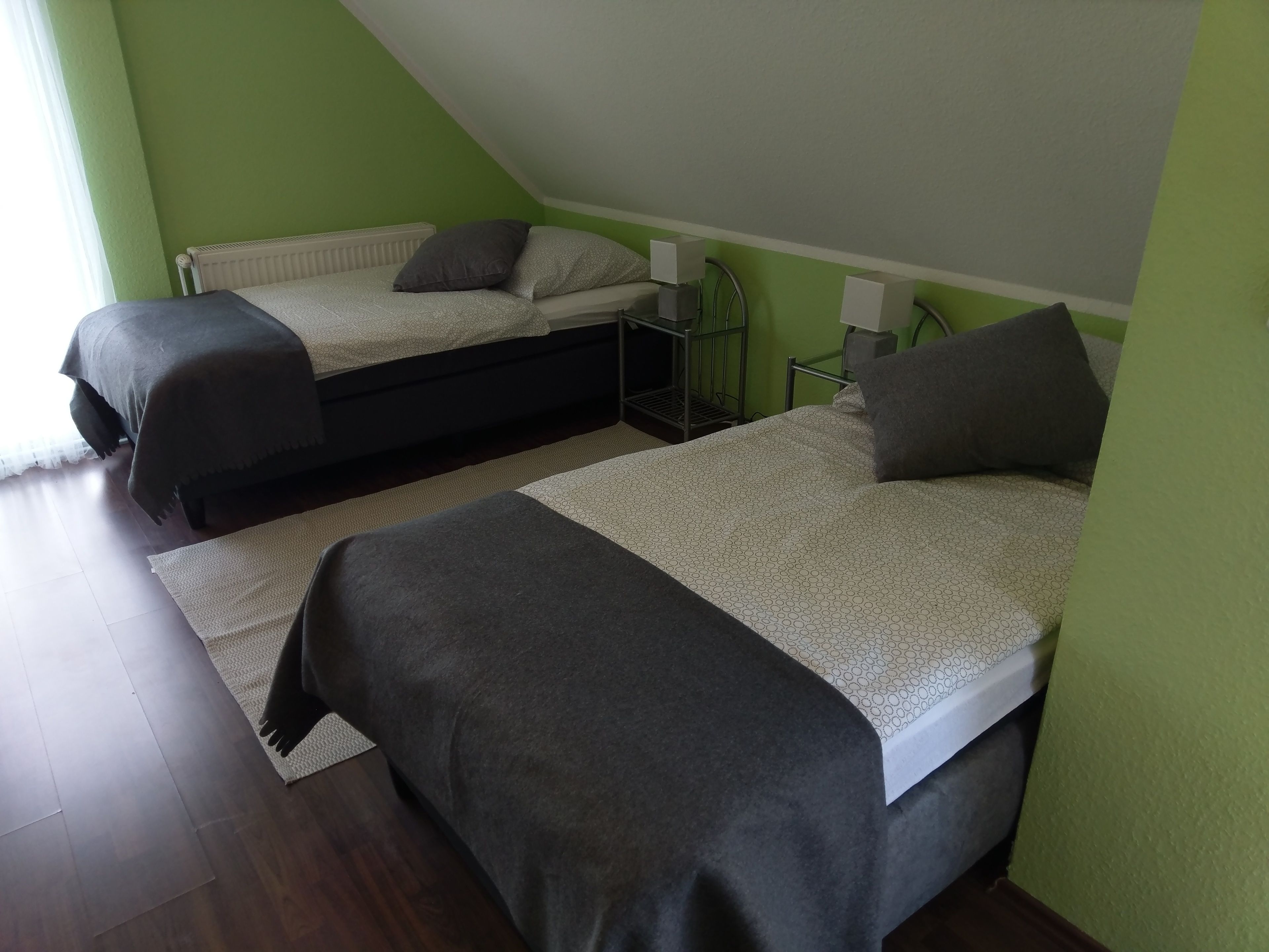 Ein Zimmer mit zwei Betten, jeweils mit einer grau-weißen Musterdecke, und einem kleinen Nachttisch mit einer Lampe.