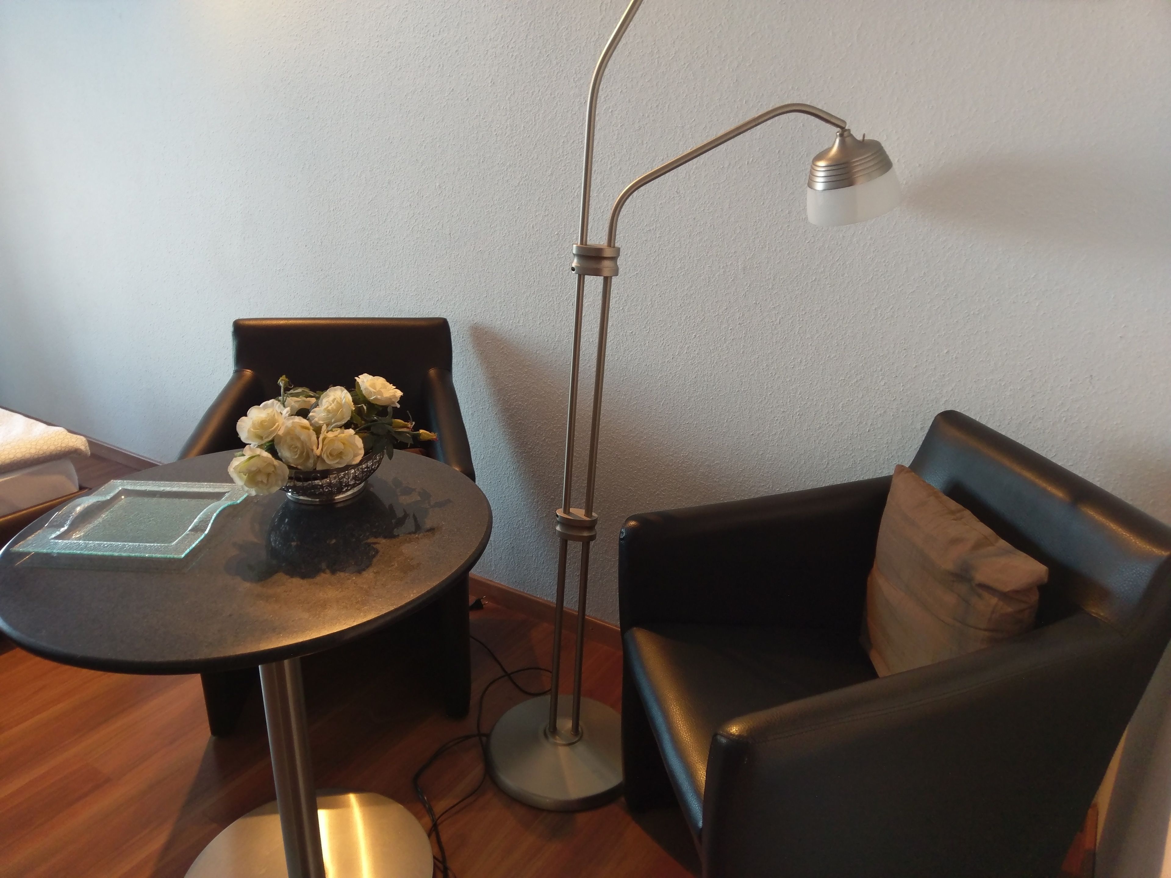 A small, modern room with a round table, a black leather sofa, and a tall floor lamp.