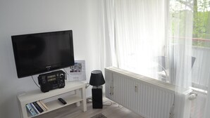 Una sala de estar moderna con un televisor de pantalla plana, una radio y una lámpara sobre una consola blanca.