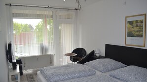Un dormitorio con cama, una silla, una mesa y una ventana con cortinas.