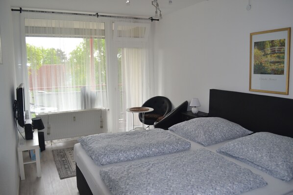 A bedroom with a bed, a chair, a table, and a window with curtains. - Ferienwohnung Resit 3 (Wunstorf)