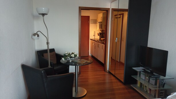 Ein modernes Hotelzimmer mit einem Bett, einem Schreibtisch mit Stuhl, einem Fernseher, einer Lampe und einem kleinen Tisch mit Blumenvase.
