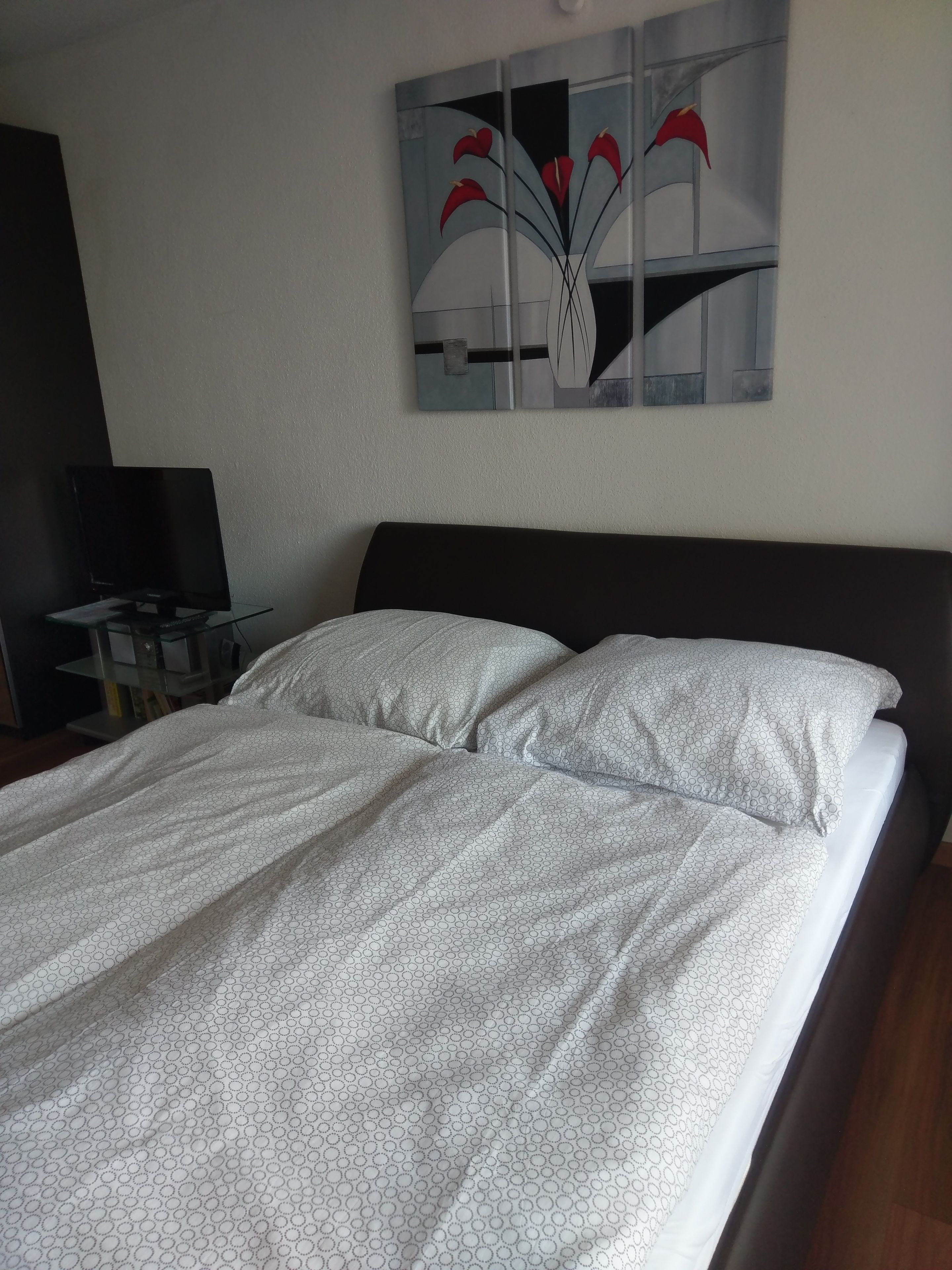 A neatly made bed with a patterned bedspread, a dark headboard, and a wall-mounted artwork above.