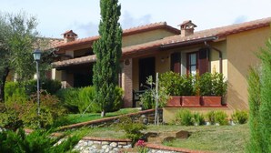 A two-story house with a tiled roof, a stone pathway, and a variety of plants and shrubs. - San Giorgio Country Residence (Santa Luce)