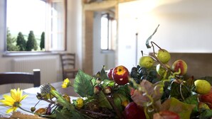 A table with a fruit arrangement and a yellow flower, a window with a view of trees, and a chair. - San Giorgio Country Residence (Santa Luce)