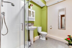 A bathroom with a glass-enclosed shower, white sink, and toilet against a green wall. - The Ship's Key Aparthotel (Londonderry)