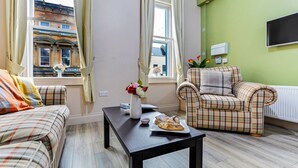 A cozy living room with a plaid sofa, a matching armchair, and a coffee table with a vase of flowers. - The Ship's Key Aparthotel (Londonderry)