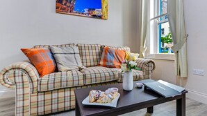 A plaid sofa with pillows, a vase with flowers, and a laptop on a table in a room with a window and a painting on the wall. - The Ship's Key Aparthotel (Londonderry)