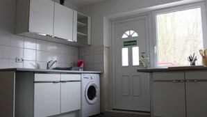 A compact kitchen with white cabinets, a washing machine, and a window with a view of trees. - ZV-Scholtz Gästehaus Eisenfelden (Winhoring)