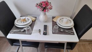 A dining table set for two with plates, cutlery, a vase with flowers, and a remote control. - ZV-Scholtz Gästehaus Eisenfelden (Winhoring)